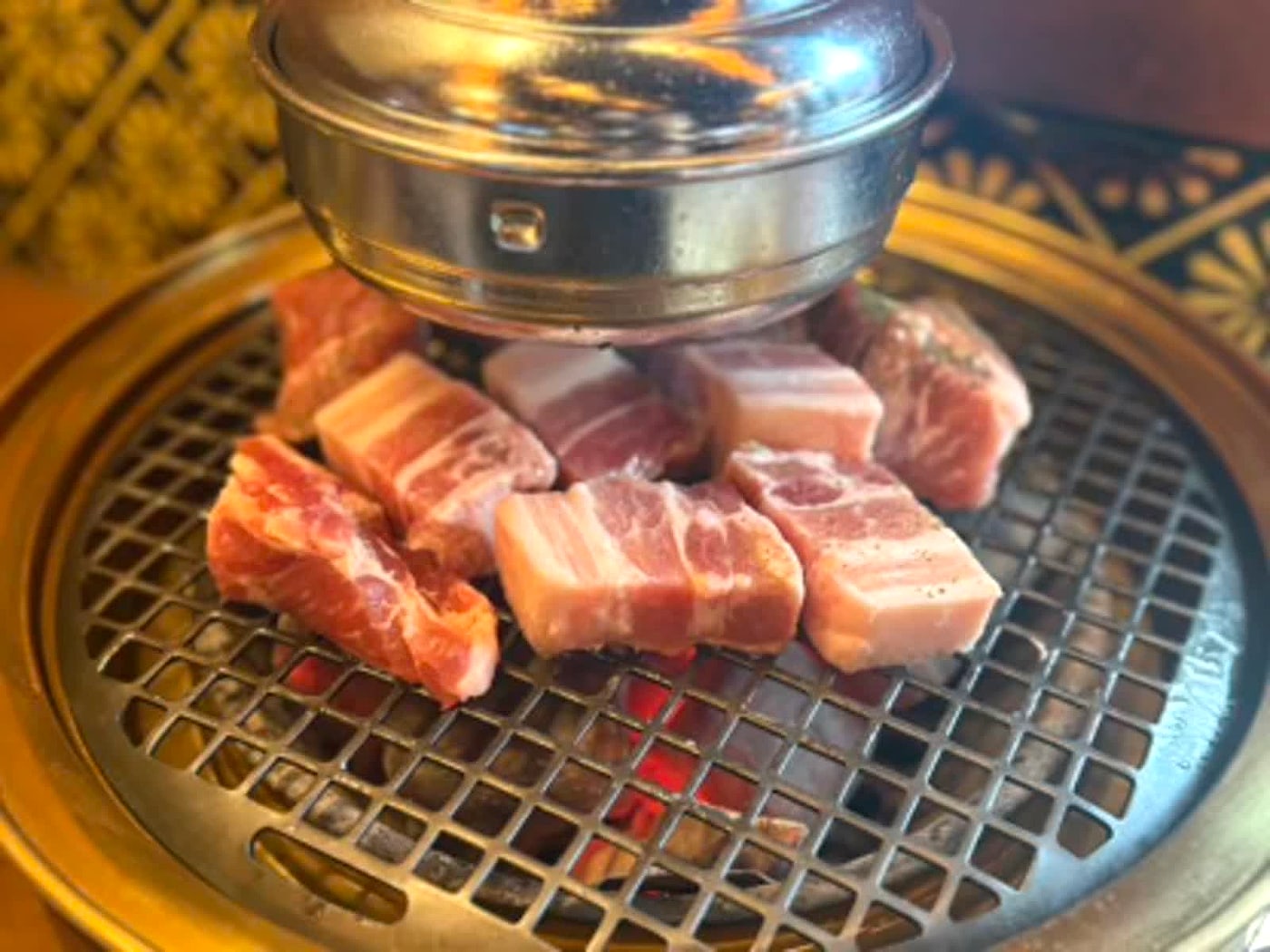 Pork pieces cooking on a Korean barbecue grill during a Hongdae dinner.