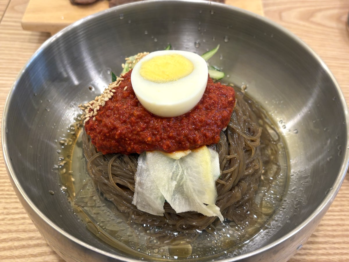 Close-up of Korean cold noodles with red spicy sauce, boiled egg, radish, and chilled broth